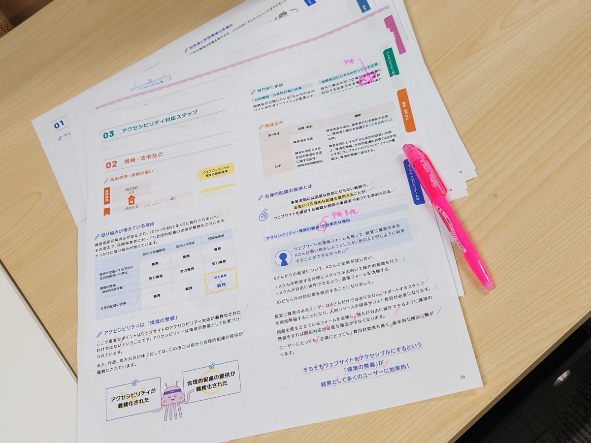 冊子「アクセシビリティってなに?」の最終稿が、机に置かれている画像。ピンクのマーカーで修正点が書き込まれている。