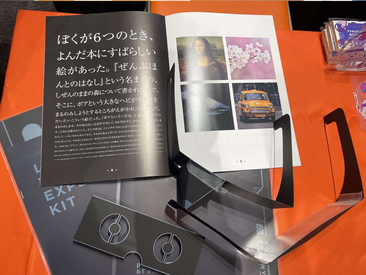 ディーゼロブースのデスクに置かれた「ロービジョン体験キット」の写真。体験メガネと、リーフレットが広げられた状態で置かれている