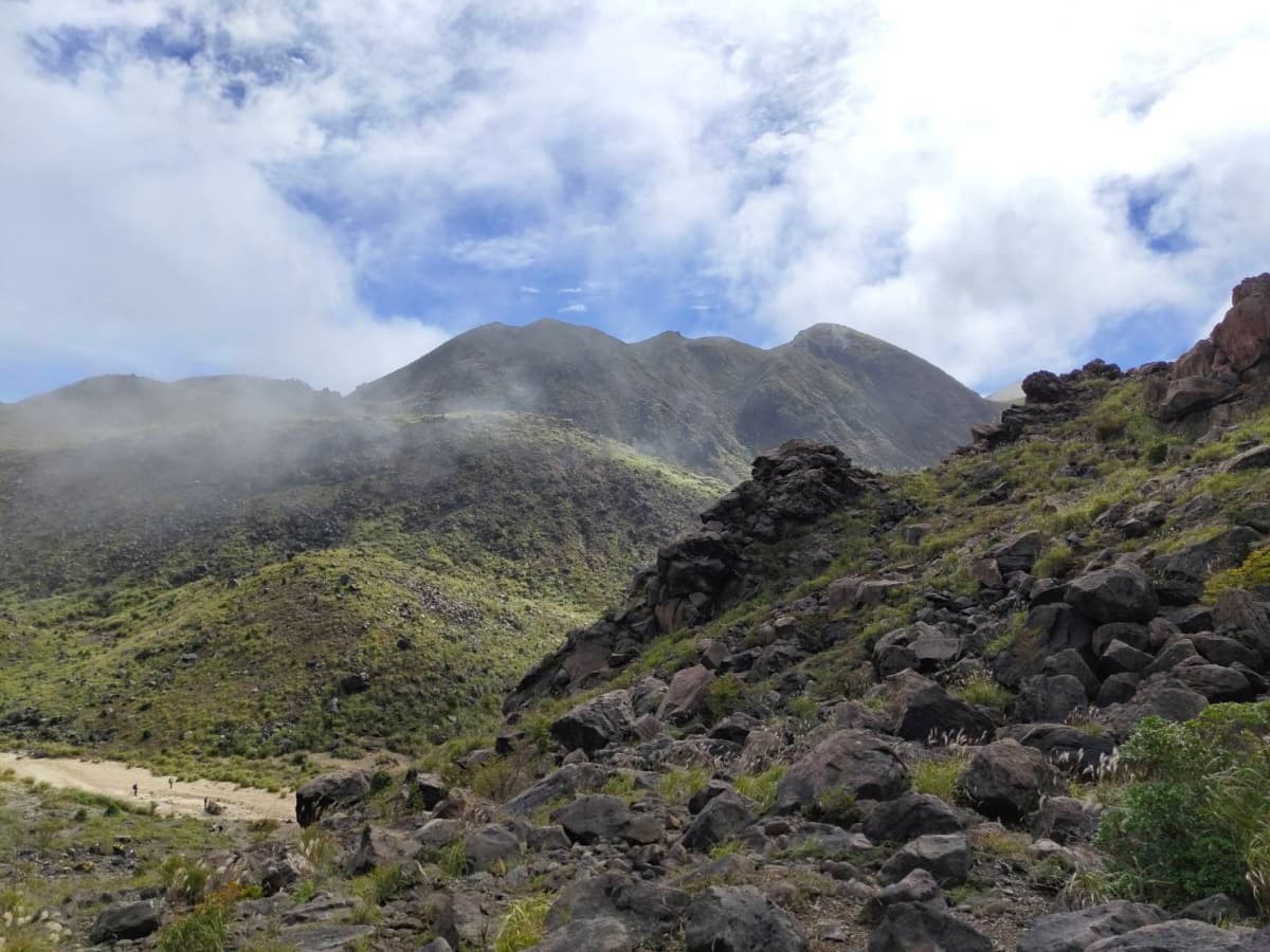 雲がうっすらかかっている三俣山。手前側にはゴツゴツした岩が転がっている。