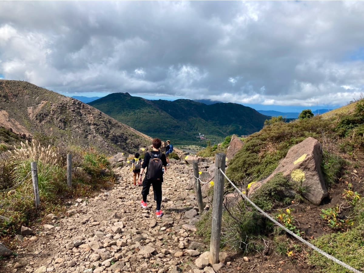 くじゅうの登山中の様子。足元にゴツゴツした石が転がっている道を登山メンバーが歩いている。