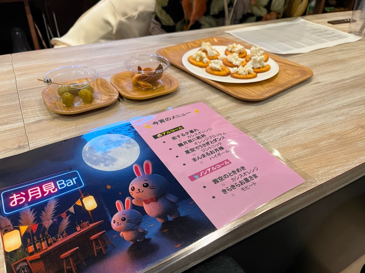 お月見Barのメニューとおつまみ。メニューには今宵のメニューと、満月と白いうさぎとお月見Barのイラストが書かれている。
