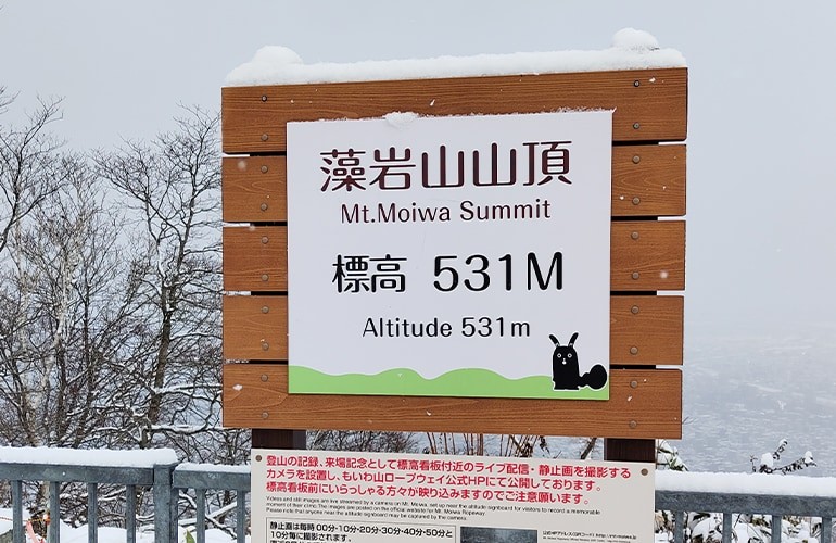 雪の積もった藻岩山山頂の看板の写真。看板には「藻岩山山頂 Mt.Moiwa Summit 標高531M Altitude 531m」と書かれている。