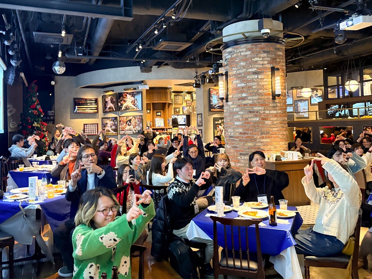 ホークスポーズを決める参加者の写真。テーブル席に座った参加者が戸惑いながらもそれぞれポーズを決めている。