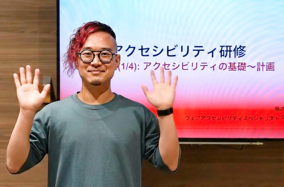 変身完了。アニメと同じ髪型・眼鏡姿の実写のゆうてんが現実世界に登場。背景はディーゼロ社内のカフェスペースに切り替わり、ゆうてんはアクセシビリティ研修のスライドの表紙が表示されているモニターの前で、両手を顔の横にあげ微笑んでいる。