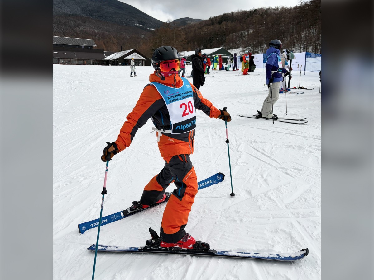 スキー場での一枚。スキーウェアを着てスキー板とポールを装備した石川さんが振り向いている。背景には他の大会参加者が見える。